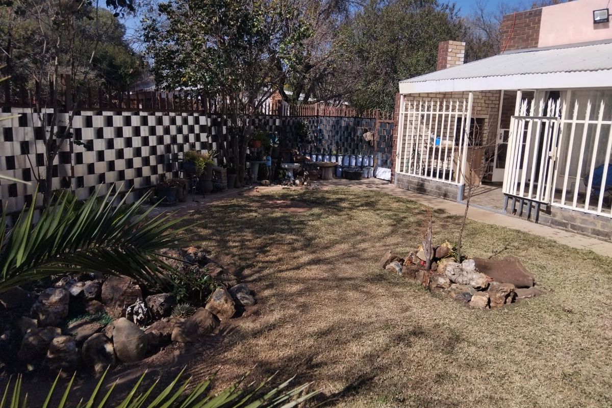 A rear garden area featuring a covered patio with security gates, a paved walkway, and a brick boundary wall.