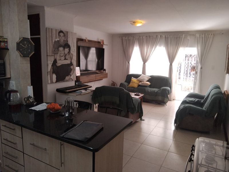 Open-plan living area featuring a kitchen with granite countertops and tiled flooring, flowing into a lounge space with direct access to a patio.