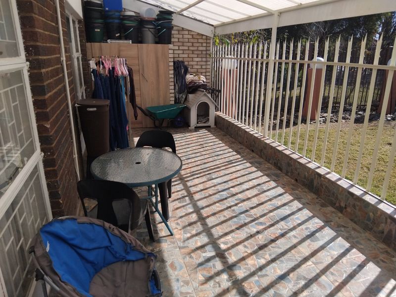 A covered patio area featuring tiled flooring, a translucent roof, and metal security fencing, providing a functional outdoor space.