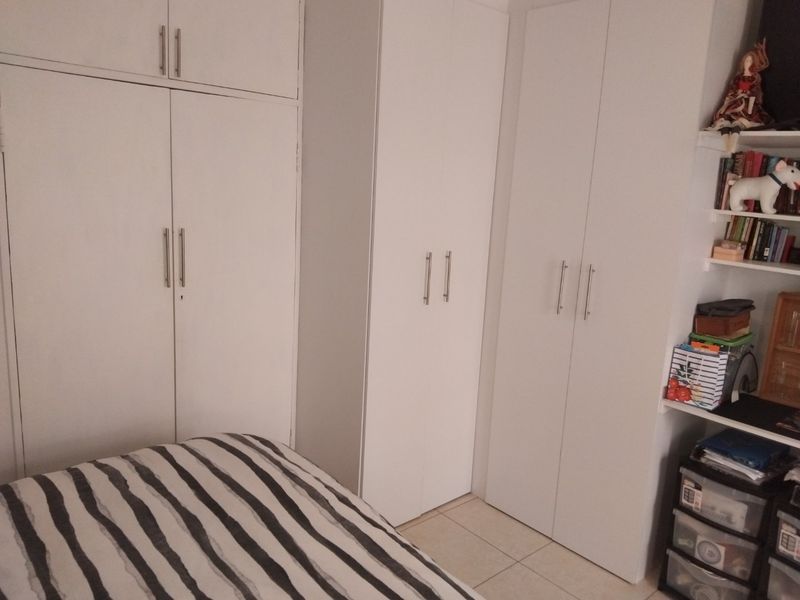 A bedroom featuring extensive white built-in cupboards providing ample storage space and neutral tiled flooring.