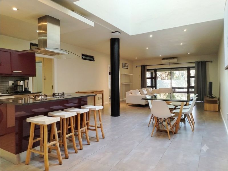 Spacious open-plan living area featuring a modern kitchen with island, gas hob, and extractor, flowing into a dining and lounge space with skylight.
