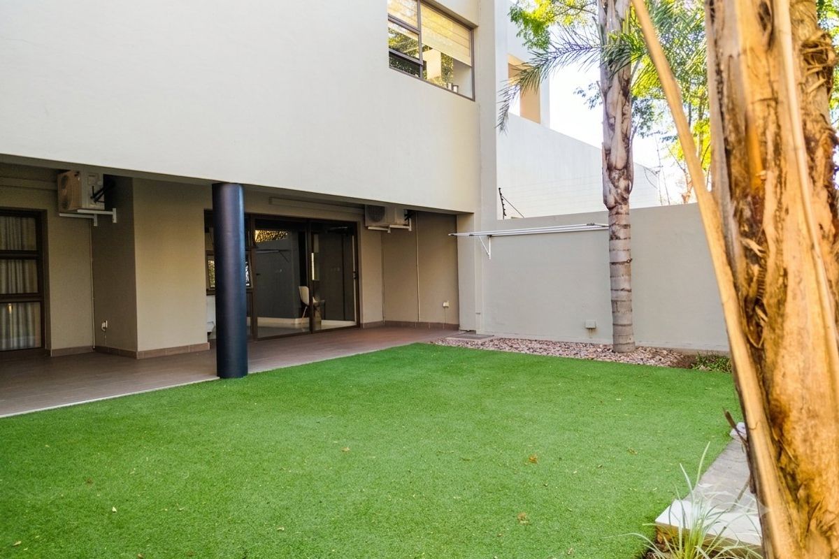 Rear exterior view featuring a covered patio area, artificial lawn, and secure boundary wall with electric fencing.