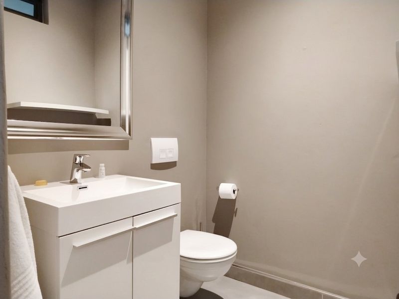 A modern guest bathroom featuring a wall-mounted toilet, a sleek white vanity cabinet with basin, and a large wall-mounted mirror.