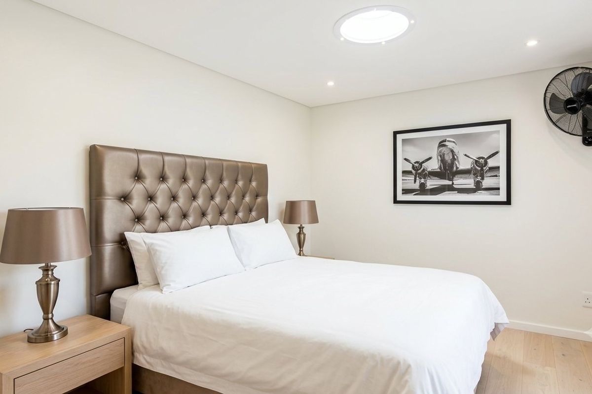 A well-maintained bedroom featuring light timber flooring, a circular skylight, recessed downlighting, and a wall-mounted fan.