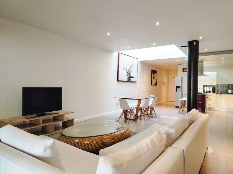 Spacious open-plan living and dining area featuring a modern kitchen, large skylight, recessed lighting, and a central structural column with neutral tiled flooring.