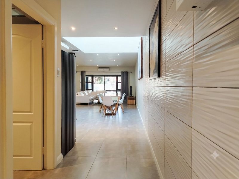 Spacious open-plan living and dining area featuring large floor tiles, a skylight, and a modern textured feature wall.