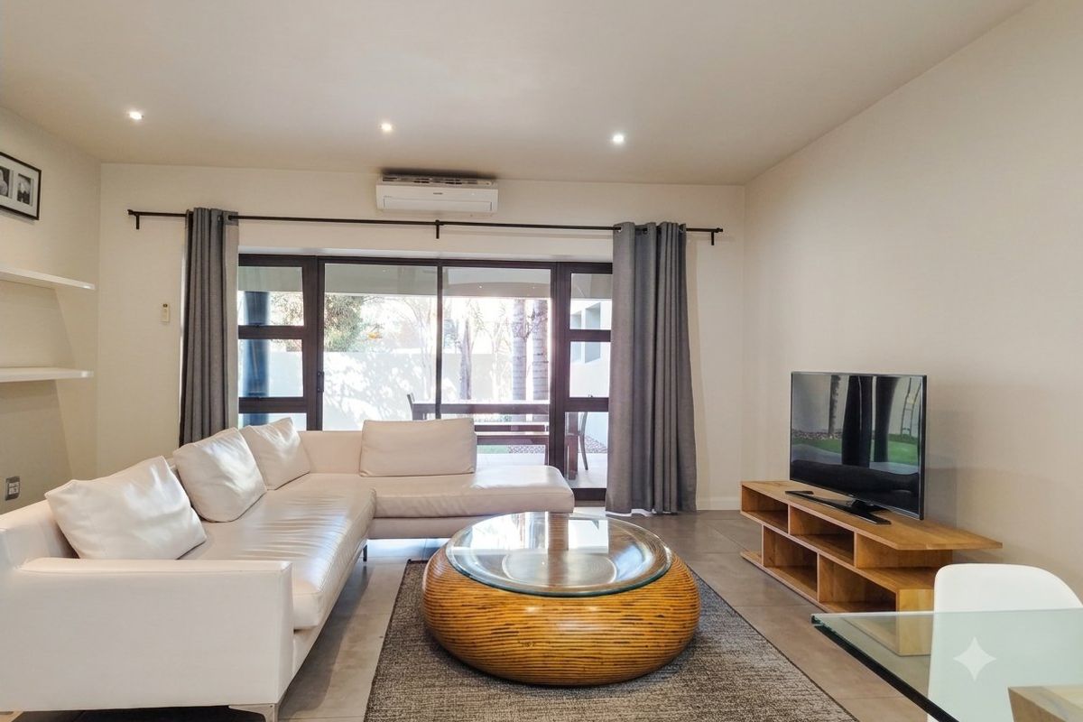 A bright and modern living room featuring tiled floors, recessed lighting, a split-system air conditioner, and large sliding glass doors leading to the patio.