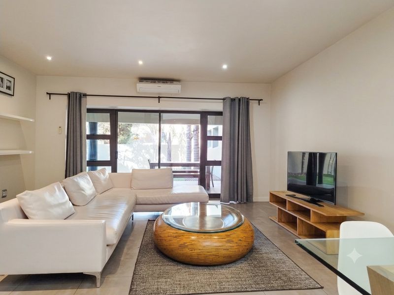 A bright and modern living room featuring tiled floors, recessed lighting, a split-system air conditioner, and large sliding glass doors leading to the patio.
