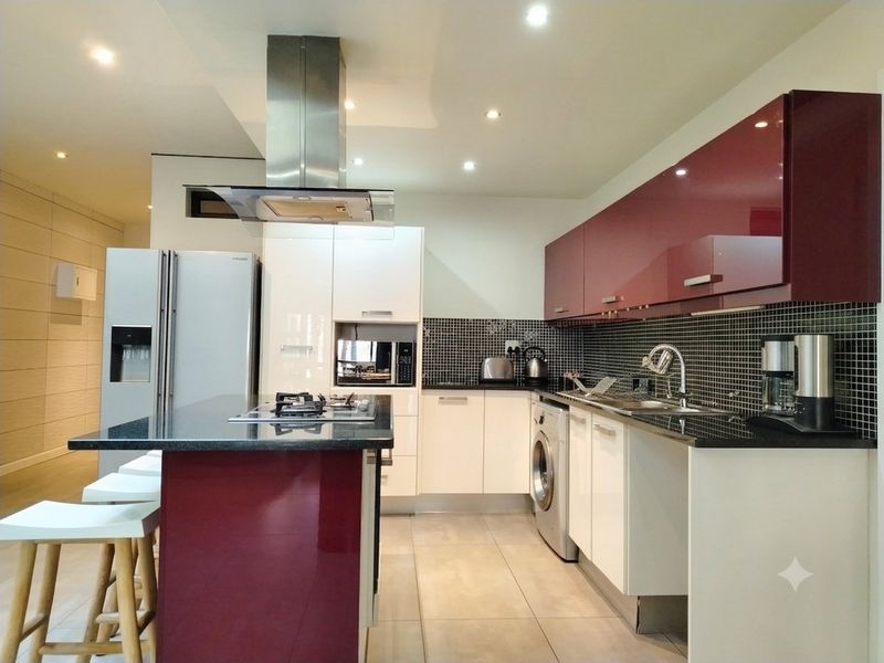 Modern kitchen featuring high-gloss cabinetry, granite countertops, a central island with a gas hob, and integrated appliances with a mosaic tile backsplash.