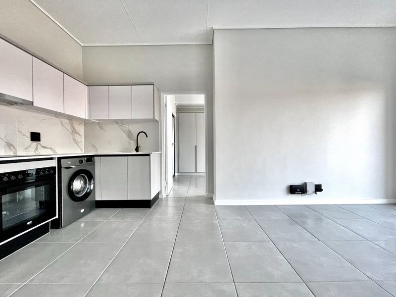 Modern open-plan kitchen featuring sleek cabinetry, marble-look splashback, built-in appliances, and neutral ceramic floor tiles, leading into a spacious living area.