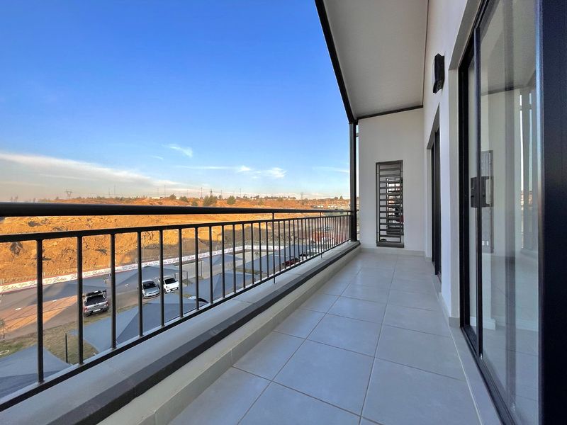 A spacious, modern balcony featuring tiled flooring, a secure metal balustrade, and large sliding glass doors, offering an open view of the surrounding area.
