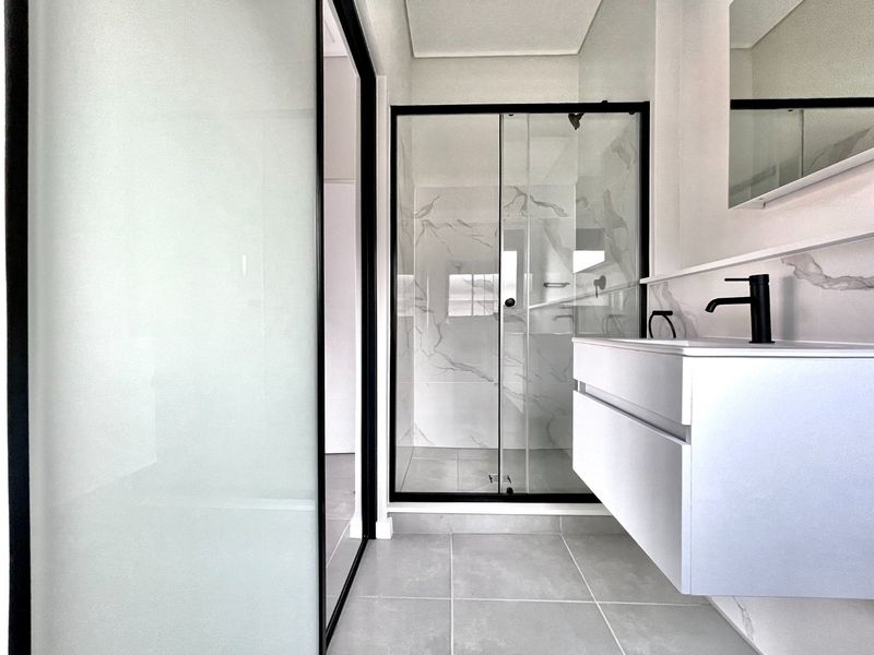 Modern bathroom featuring a floating vanity, black matte fixtures, and a glass-enclosed shower with marble-look wall tiling.
