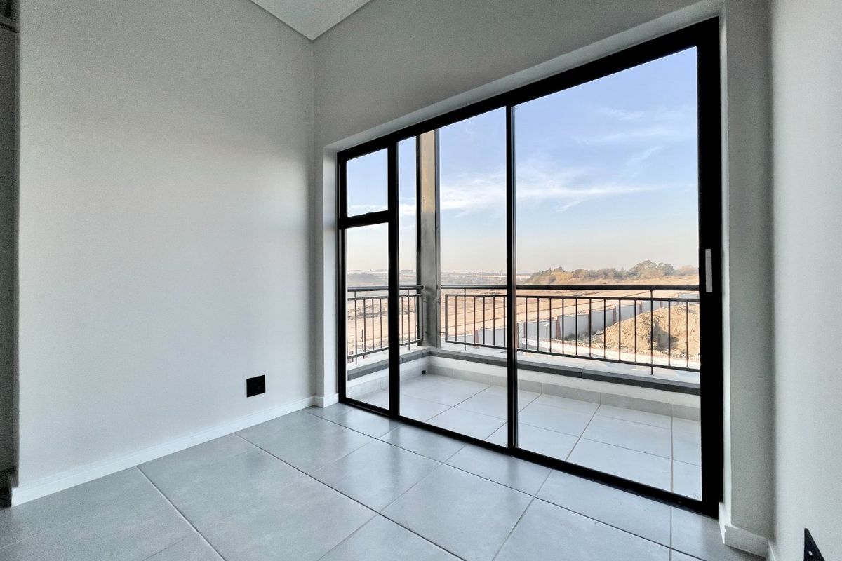 A bright, empty living area featuring large sliding glass doors that open onto a private balcony with scenic views.