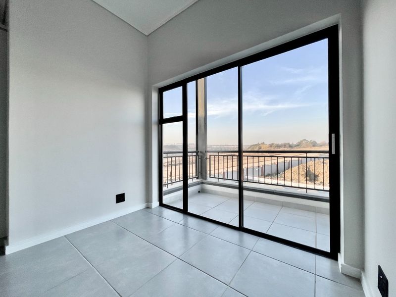 A bright, empty living area featuring large sliding glass doors that open onto a private balcony with scenic views.