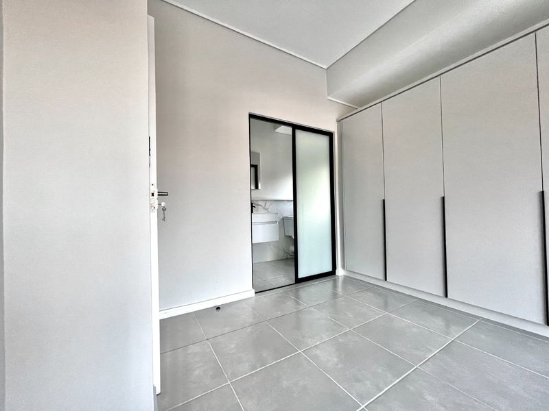 Modern bedroom featuring neutral tiled flooring, extensive built-in cupboards with sleek handles, and a sliding door leading to an en-suite bathroom.