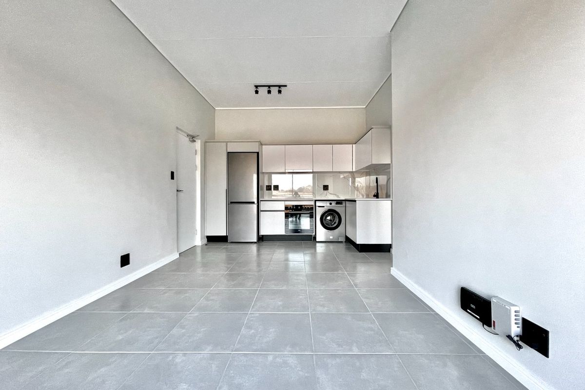 Modern open-plan living area featuring a sleek kitchen with built-in cabinetry, integrated appliances, and neutral tiled flooring throughout.