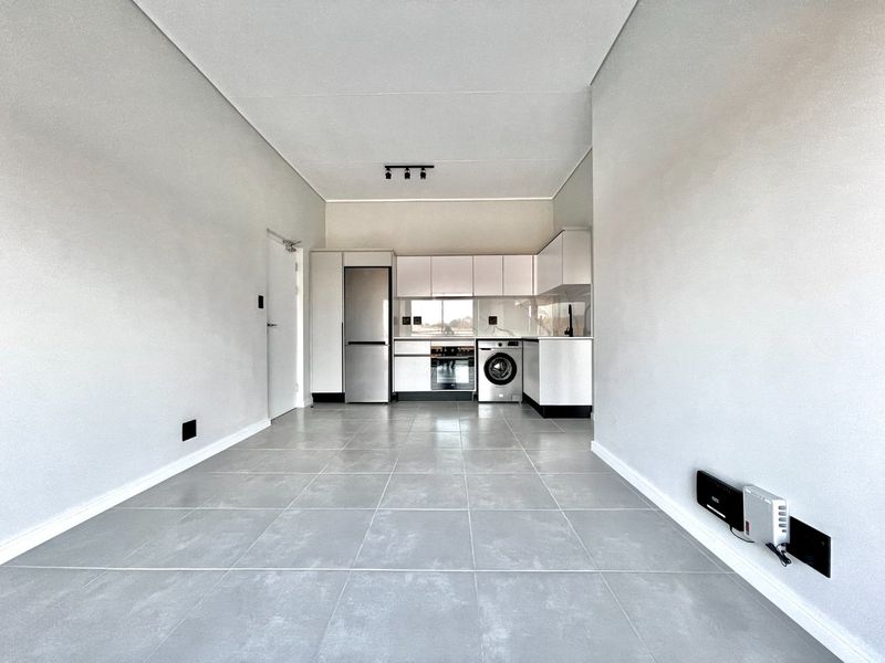 Modern open-plan living area featuring a sleek kitchen with built-in cabinetry, integrated appliances, and neutral tiled flooring throughout.