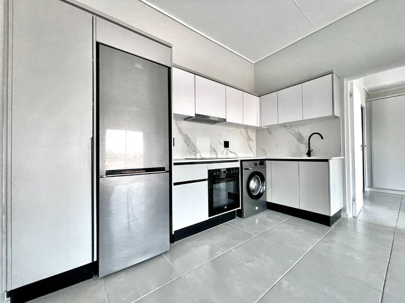 Modern kitchen featuring sleek white cabinetry, marble-look splashback, integrated oven, extractor fan, and high-quality tiled flooring.