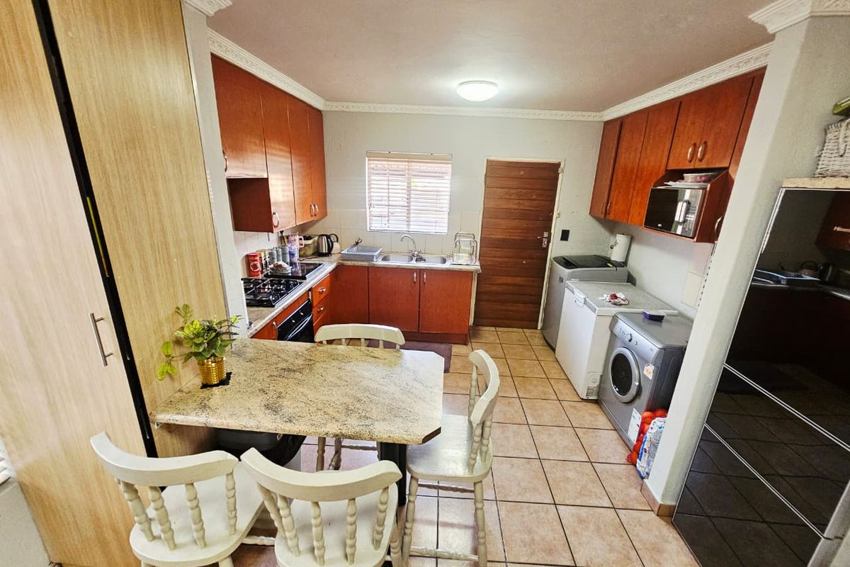 A functional kitchen featuring wooden cabinetry, tiled flooring, a gas hob, and an integrated dining nook, providing a practical layout for daily meal preparation.