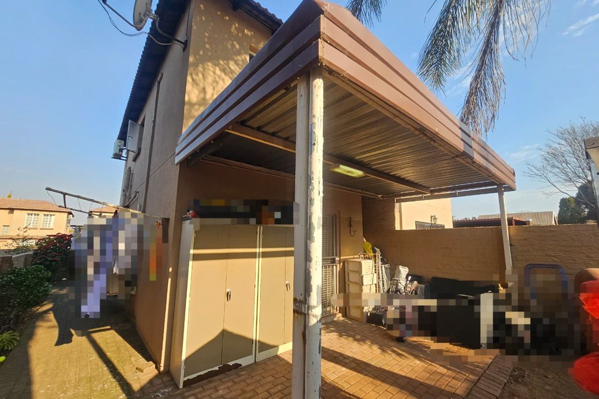 Rear exterior view of the townhouse featuring a covered patio area with paved flooring and a metal support structure.