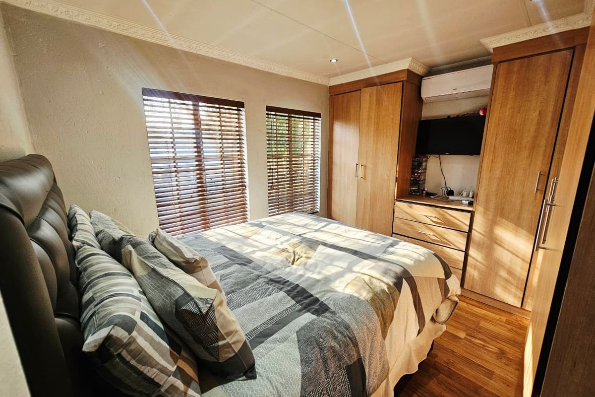 A well-maintained bedroom featuring built-in wooden cupboards, laminate flooring, recessed downlighting, and an integrated air conditioning unit.