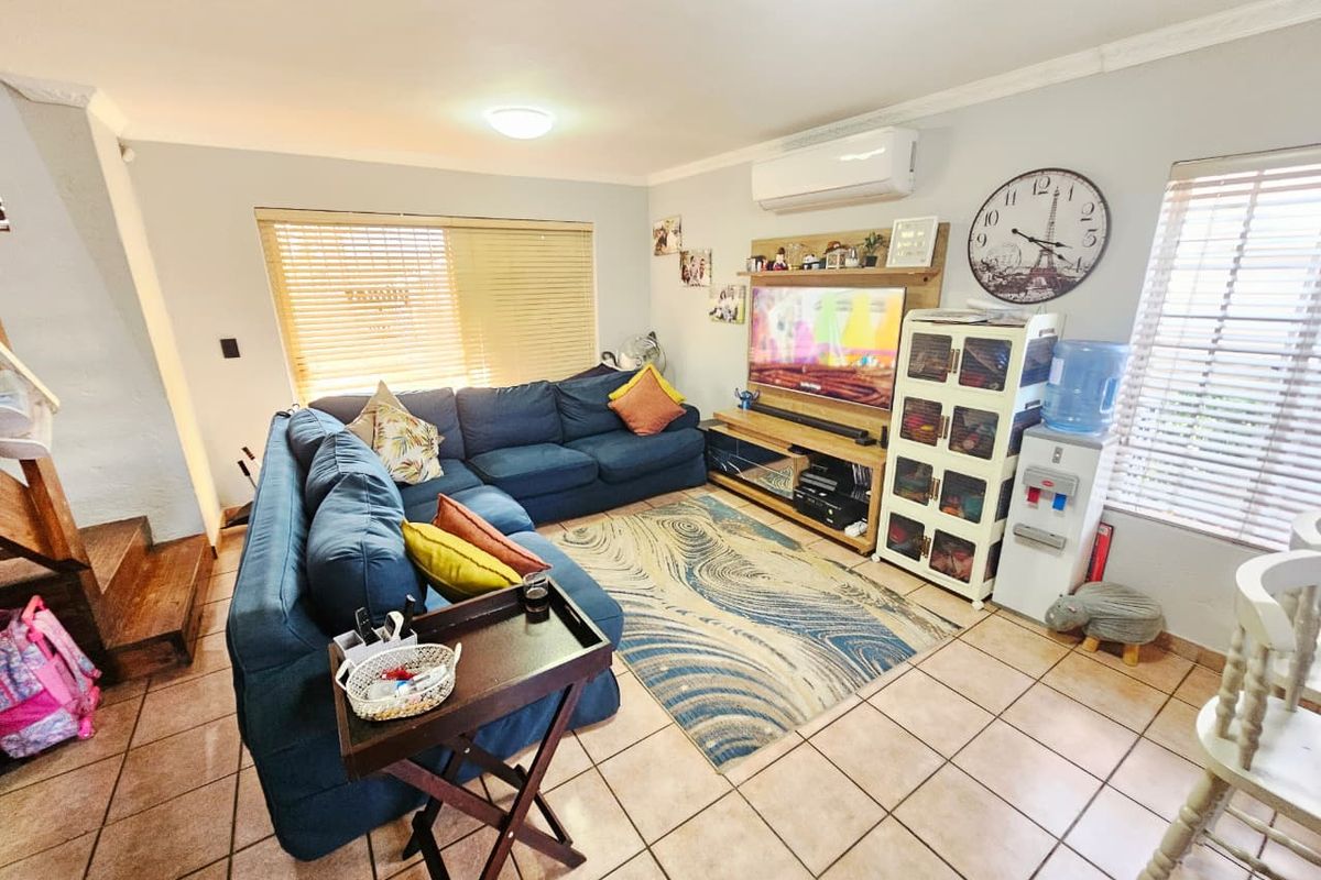 A comfortable living room featuring tiled flooring, split-system air conditioning, and large windows with venetian blinds, providing a functional and well-lit space.