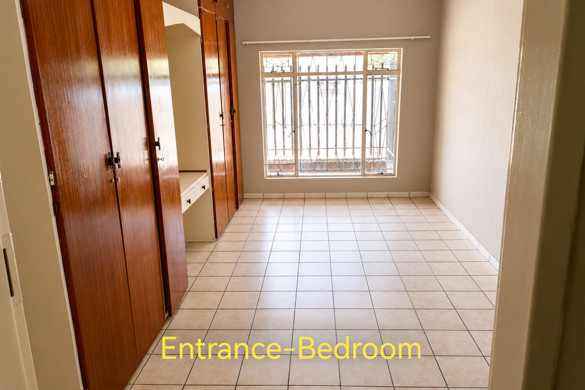 An empty bedroom featuring tiled flooring, built-in wooden cupboards, and a built-in vanity desk, with security bars installed on the window.