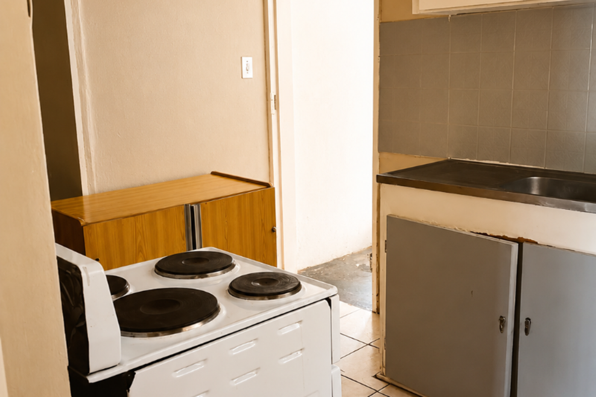 A functional kitchen featuring tiled flooring, a stainless steel sink, and built-in cabinetry, currently showing signs of wear and requiring cosmetic updates.
