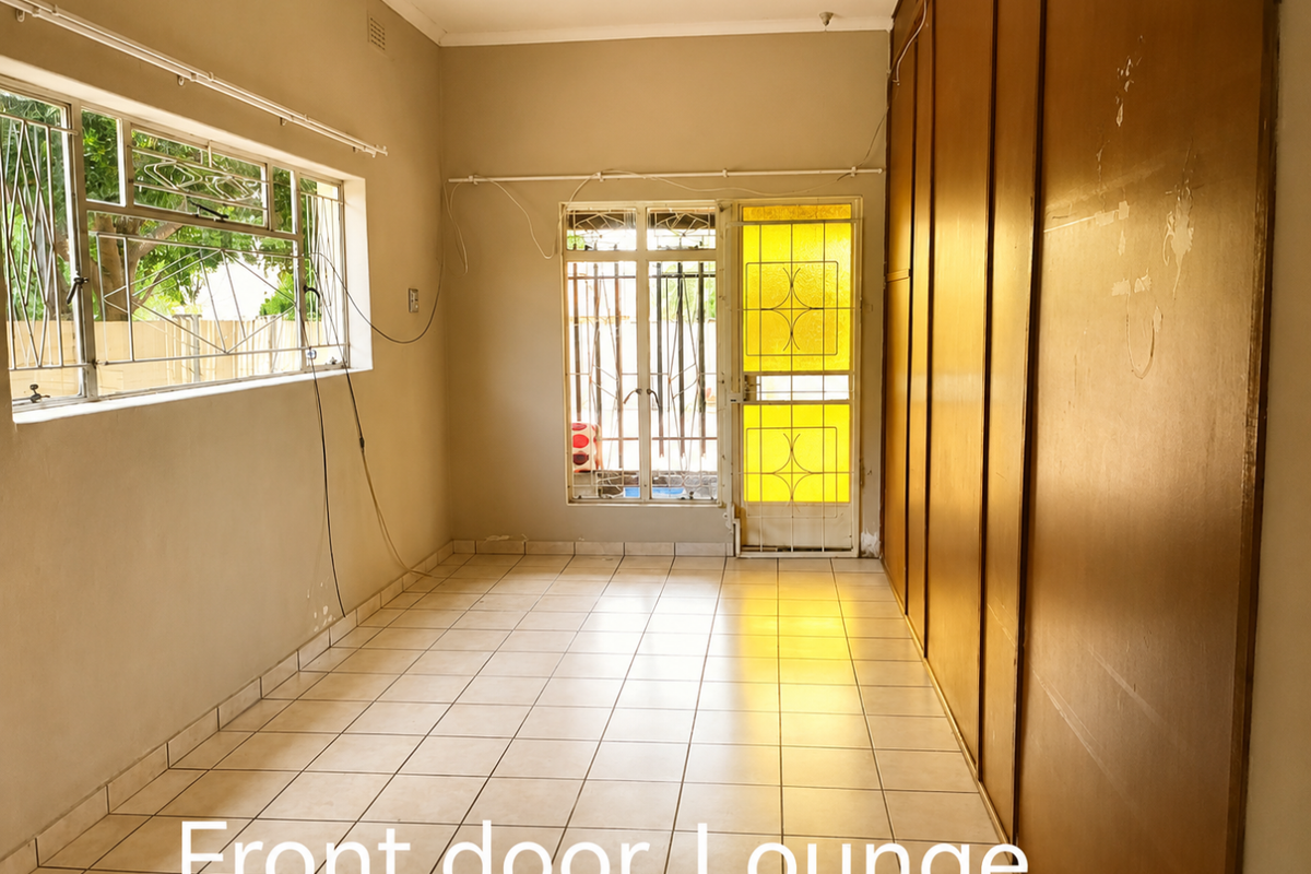 An empty lounge area featuring tiled flooring, built-in storage cupboards, and a security gate leading to the exterior.