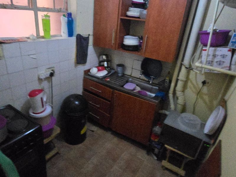 A compact, dated kitchen featuring built-in cabinetry, a stainless steel sink, and tiled splashbacks, requiring modernization and improved finishes.