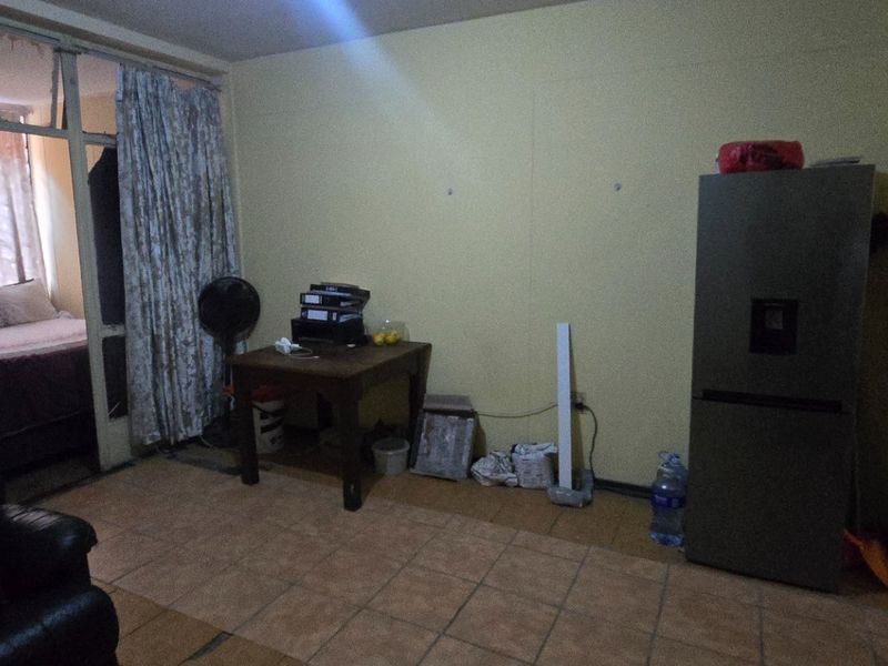 An open-plan living area featuring tiled flooring and a partitioned bedroom access, requiring cosmetic updates to improve the overall aesthetic and brightness.