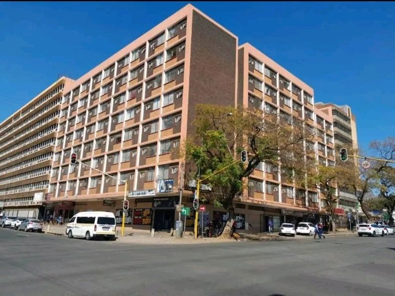 A multi-story apartment building featuring ground-floor retail spaces, situated on a prominent street corner in an urban setting.