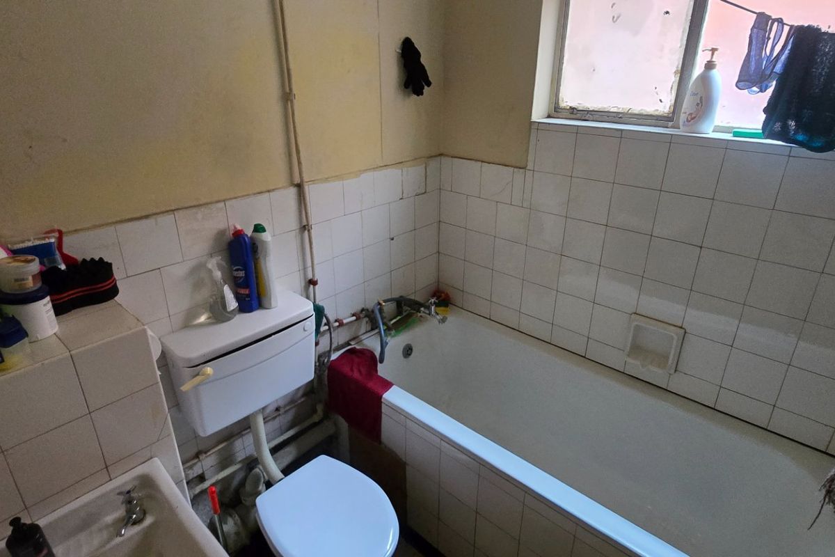 A dated bathroom featuring a standard bathtub, toilet, and wall tiling, currently requiring significant cosmetic updates and modernization of fixtures.