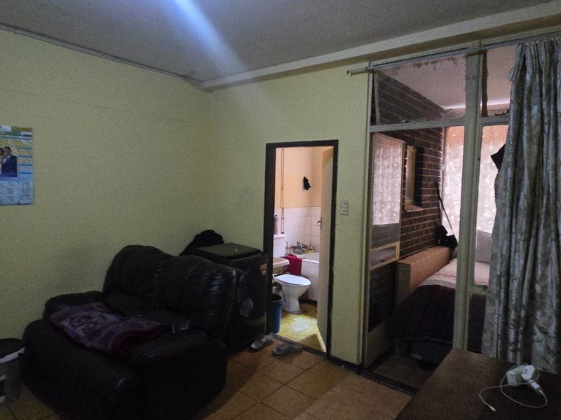Open plan living area featuring tiled flooring, with direct access to an adjoining bathroom and bedroom space through a glass partition.