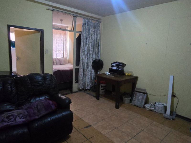 A living area featuring tiled flooring and access to an adjacent bedroom through a sliding glass door, requiring cosmetic updates to improve the space.