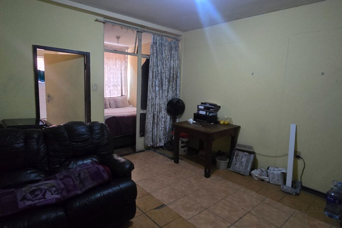 A living room area featuring tiled flooring and access to an adjacent bedroom, requiring cosmetic updates to improve the overall aesthetic and condition.