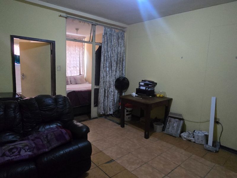 A living room area featuring tiled flooring and access to an adjacent bedroom, requiring cosmetic updates to improve the overall aesthetic and condition.