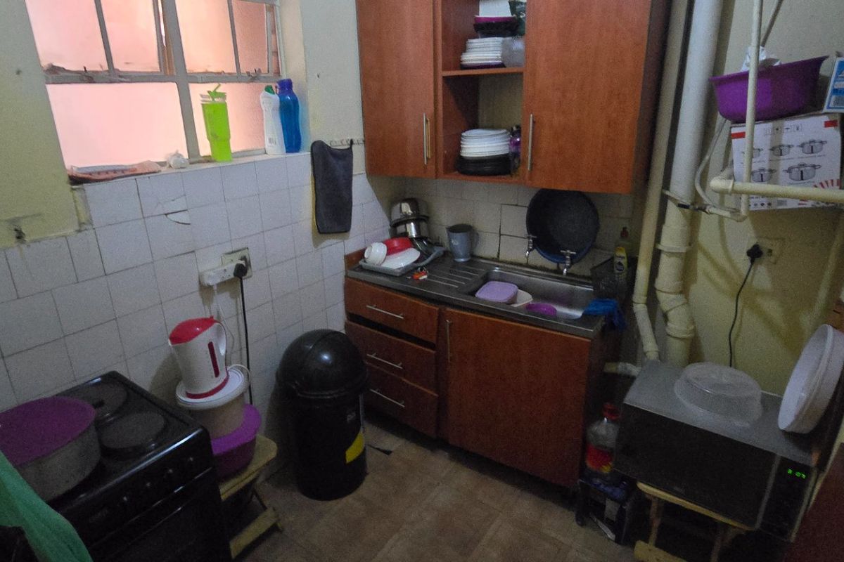 Compact kitchen area featuring built-in cabinetry, a stainless steel sink, and tiled splashback, requiring cosmetic updates and improved finishings.