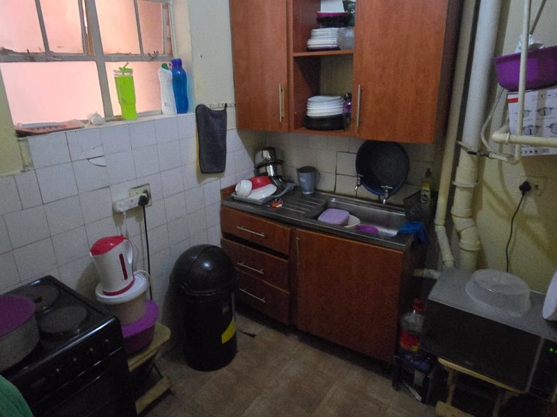 Compact kitchen area featuring built-in cabinetry, a stainless steel sink, and tiled splashback, requiring cosmetic updates and improved finishings.