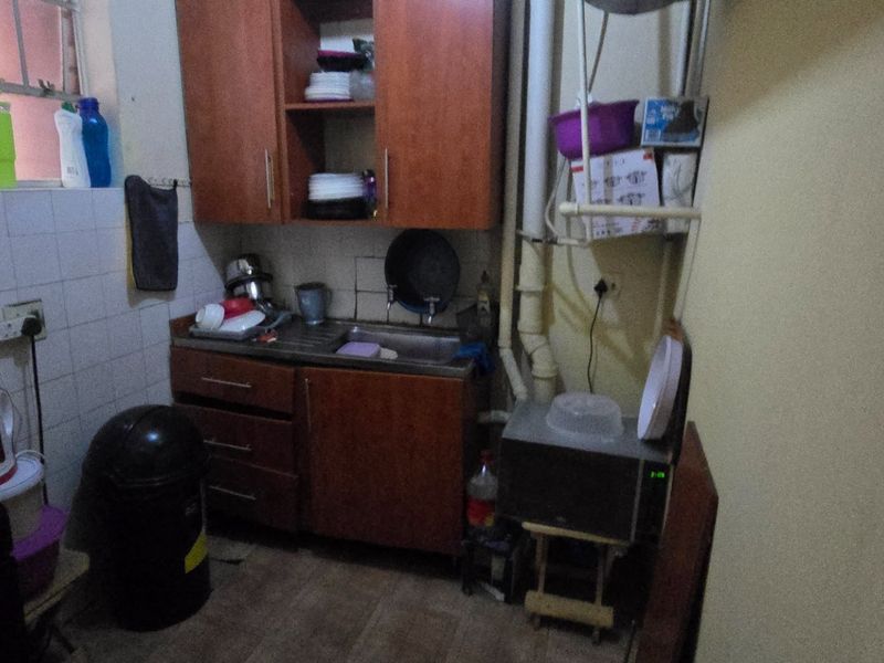 A compact kitchen area featuring wooden cabinetry, a stainless steel sink, and tiled splashbacks, requiring cosmetic updates and improved plumbing concealment.