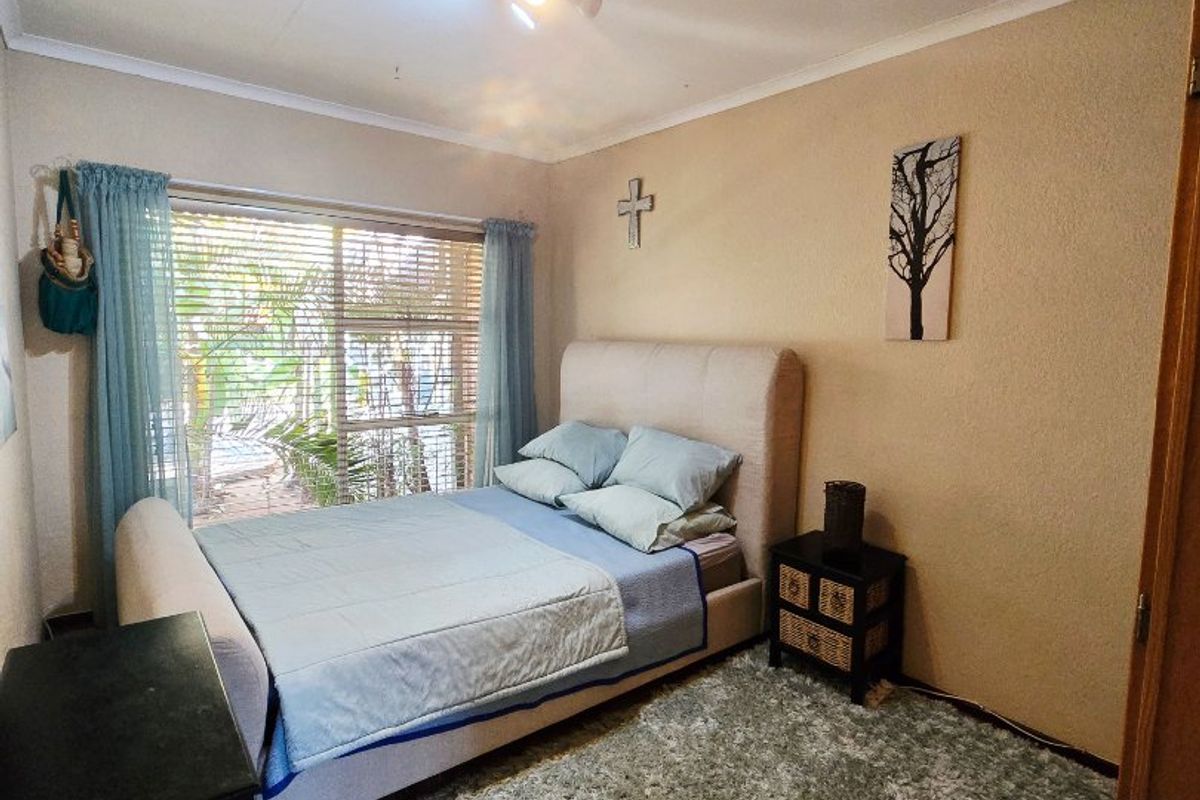 A cozy bedroom featuring a large window with venetian blinds, neutral wall finishes, and a central ceiling light fixture.
