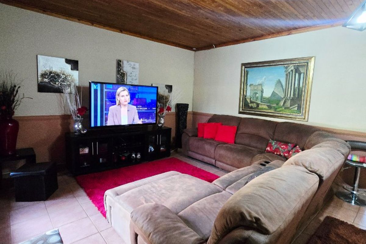 A comfortable living room featuring a warm timber tongue and groove ceiling, ceramic tiled flooring, and a practical two-tone wall finish.