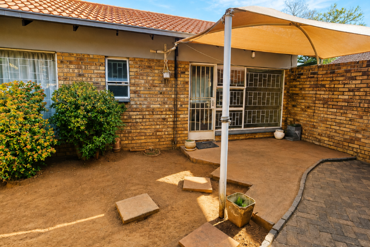 Rear exterior view featuring a brick facade, tiled roof, paved walkway, and a shade sail over a patio area.