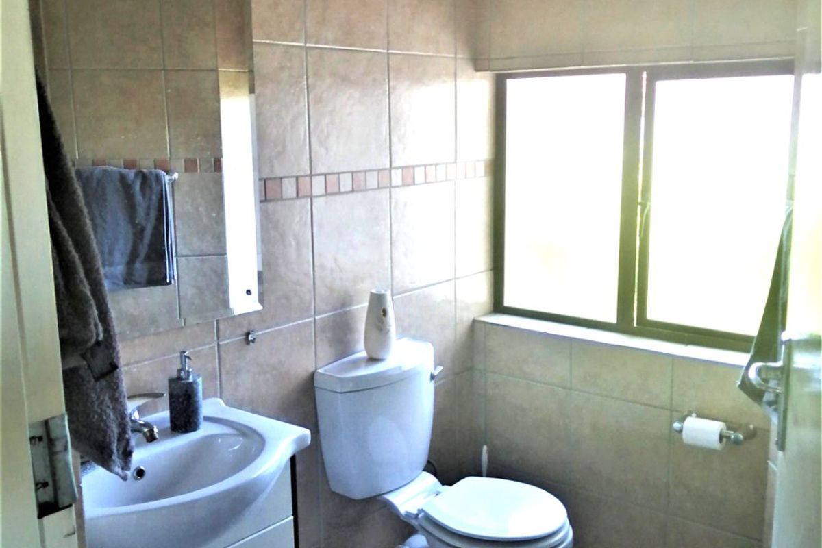 A functional bathroom featuring tiled walls and flooring, a vanity cabinet with a basin, and a toilet positioned under a window.