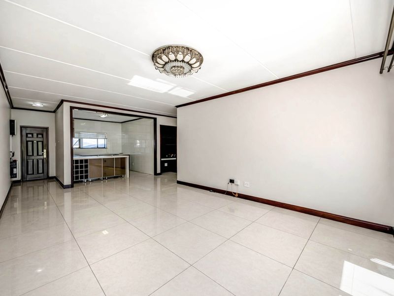 Spacious open-plan living area featuring polished porcelain floor tiles, neutral walls, and an integrated kitchen space with built-in cabinetry.