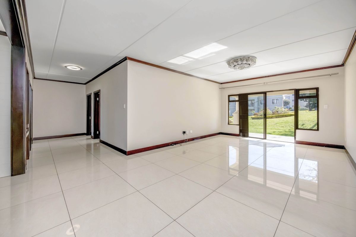 A spacious, bright, and empty living area featuring large format floor tiles, timber trim, and sliding glass doors leading to a garden view.