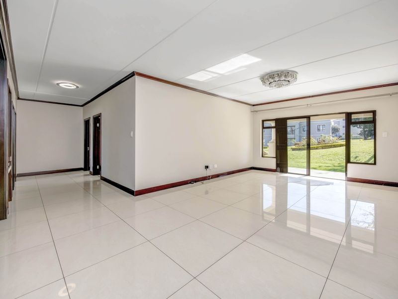 A spacious, bright, and empty living area featuring large format floor tiles, timber trim, and sliding glass doors leading to a garden view.