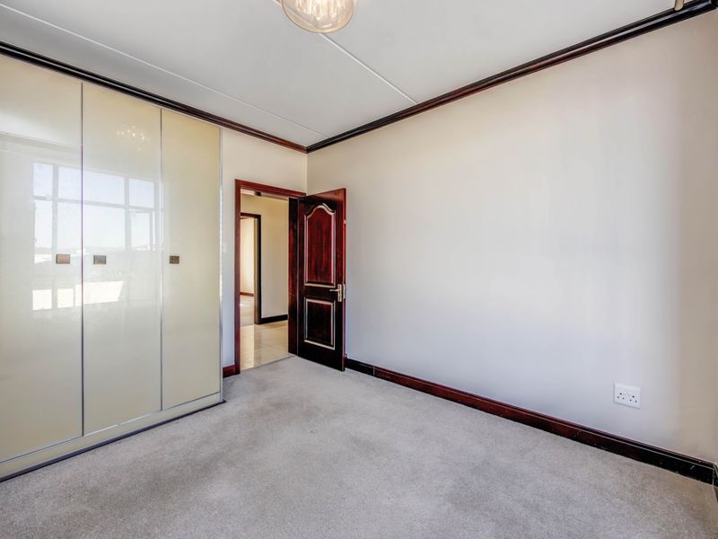 An empty bedroom featuring neutral carpeting, built-in wardrobes with sliding doors, and dark timber trim detailing.