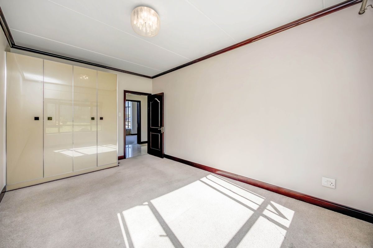 A bright, empty bedroom featuring neutral carpeting, built-in cupboards, and dark wood trim detailing.