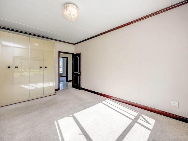 A bright, empty bedroom featuring neutral carpeting, built-in cupboards, and dark wood trim detailing.